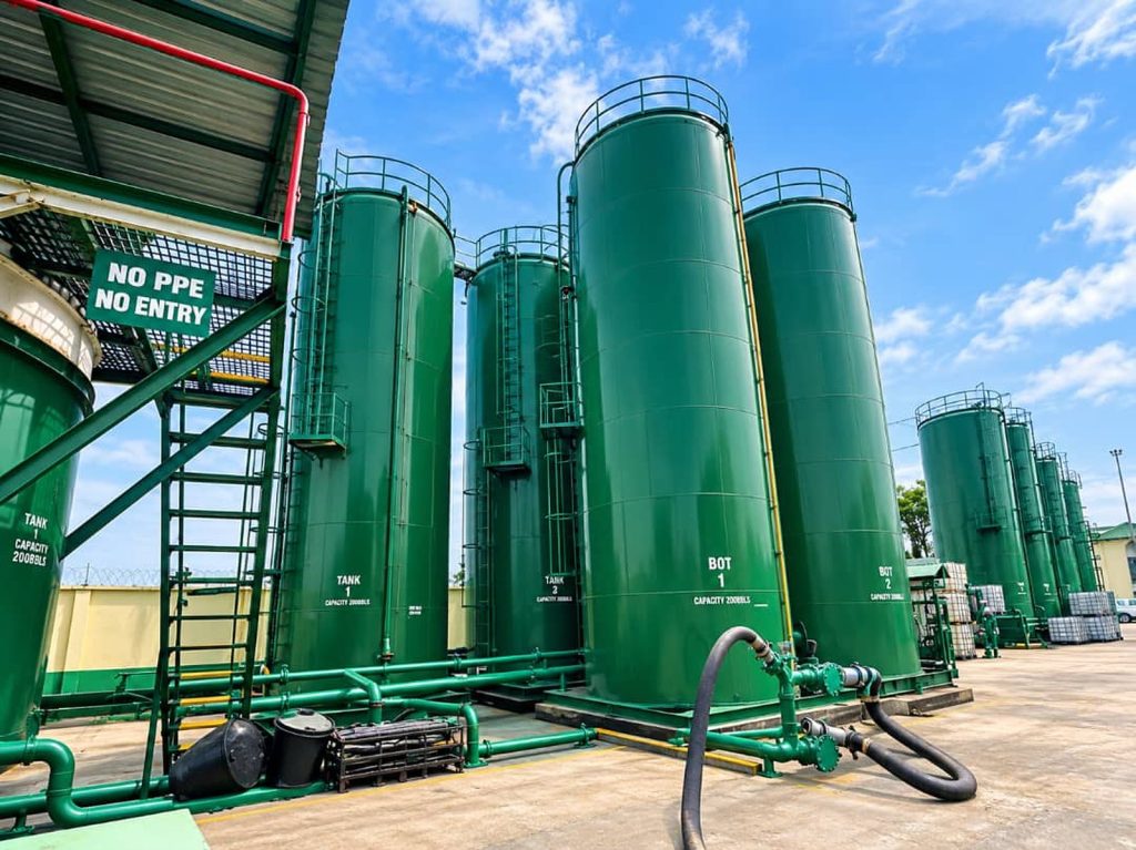 Oilchem tank farm with rows of tall green storage tanks and transfer pipework